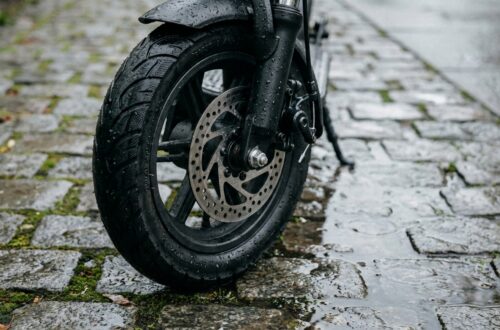 Zbliżenie na koło hulajnogi na mokrej kostce, widoczna opona i hamulec, naturalne światło.