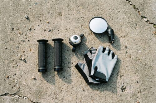 Zestaw akcesoriów hulajnogi ułożony na betonie: gripy, dzwonek, lusterko, rękawiczki.